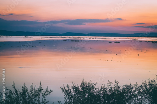 Fototapeta Naklejka Na Ścianę i Meble -  long exposure vanilla colorful sky and  lake reflection with mountains in the background. blurred wild grass blowing in the wind on foreground