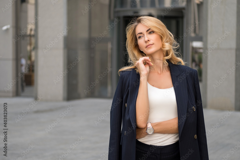 Beautiful blonde woman in navy blue classic smart-casual outfit outdoors near hi-tech business building. Space for text.