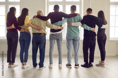 Team of confident diverse people standing, looking out window together and hugging ready to always support each other. Group of mixed-race friends or colleagues showing unity and mutual responsibility photo