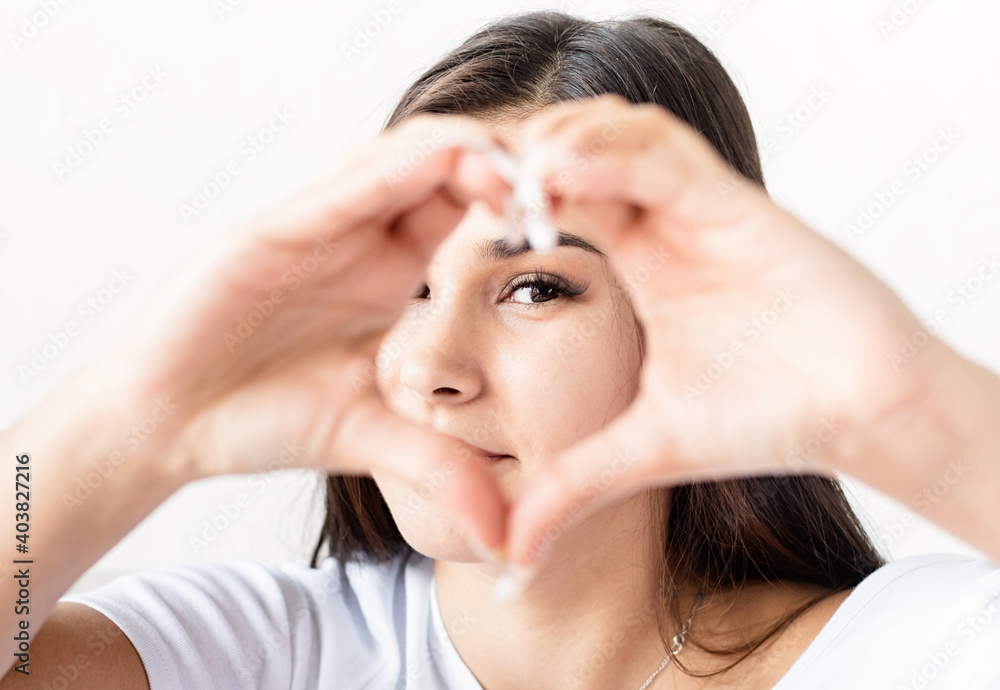 Young happy brunette woman in white t-shirt showing heart sign with her hands in front of face Young happy brunette woman in white t-shirt showing heart sign with her hands in front of face