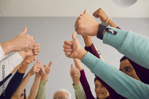 Diverse mixed-race group of people celebrating successful work results and giving thumbs-up. Multiethnic team showing unity, raising hands, making unanimous decision together and voting for good idea