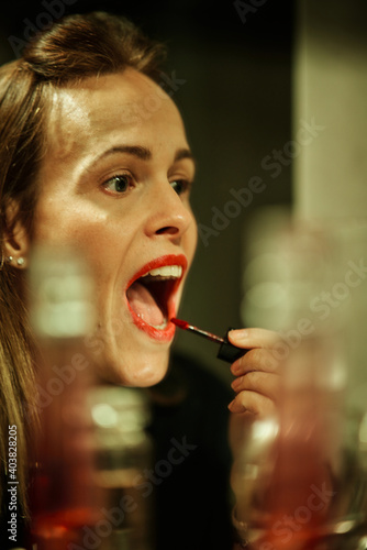 young woman with its mouth open and painting her lips in front of the mirror