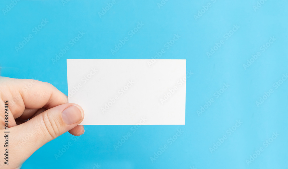 Hand holds a blank white business card on a blue background Hand holds a blank white business card on a blue background