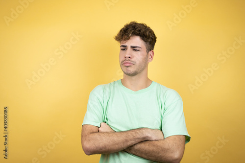 Handsome man wearing a green casual t-shirt over yellow background thinking looking tired and bored with crossed arms