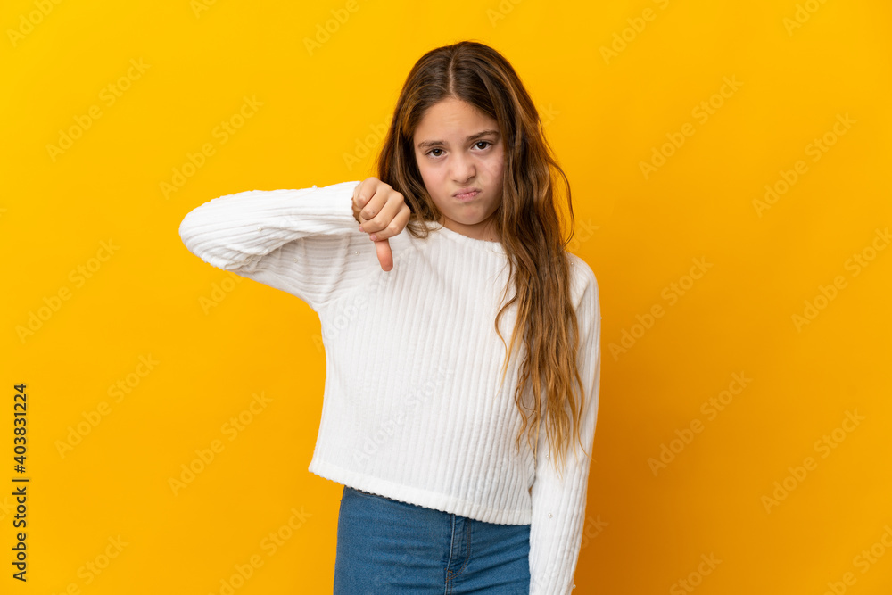 Child over isolated yellow background showing thumb down with negative expression Child over isolated yellow background showing thumb down with negative expression