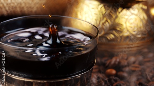 Drop of Turkish coffee falling in glass cup.