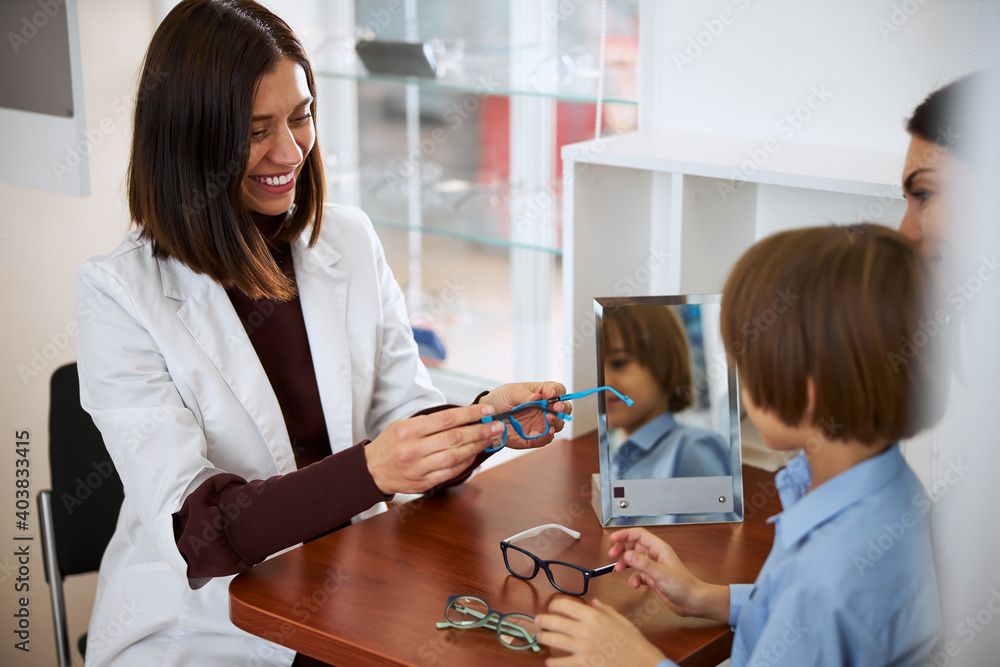 Fototapeta premium Friendly medical assistant presenting blue glasses to a kid