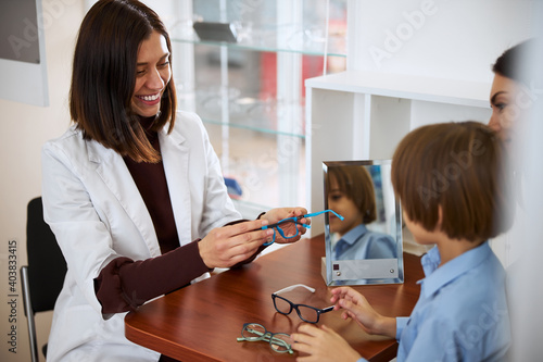 Friendly medical assistant presenting blue glasses to a kid