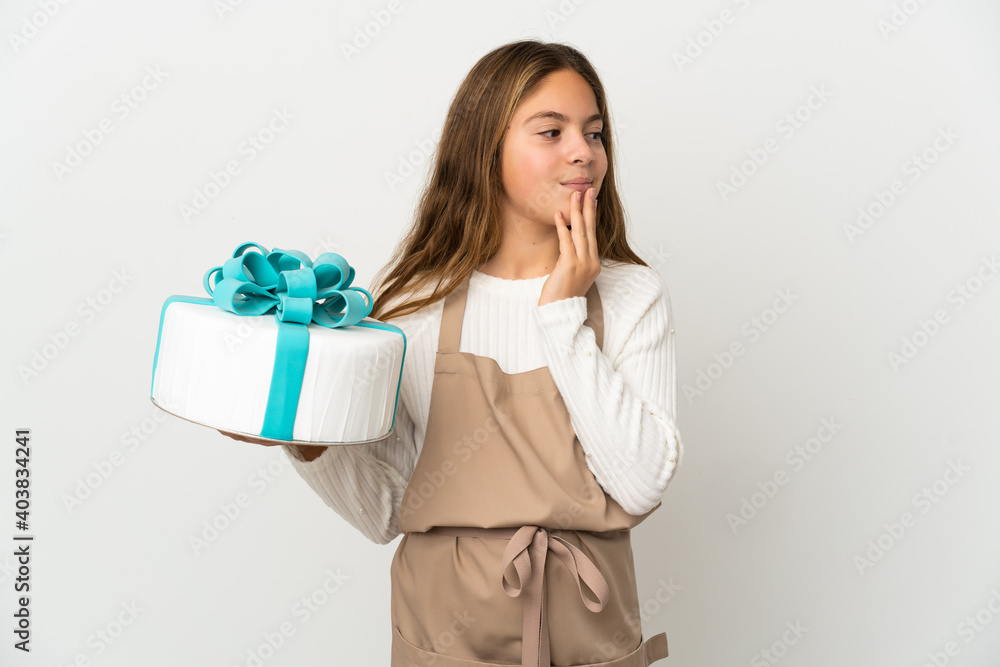 Little girl holding a big cake over isolated white background looking up while smiling Little girl holding a big cake over isolated white background looking up while smiling