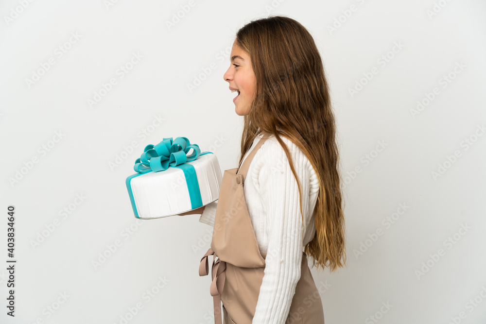 Little girl holding a big cake over isolated white background laughing in lateral position Little girl holding a big cake over isolated white background laughing in lateral position