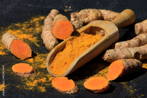 Turmeric powder in a wooden spoon and roots on a dark table (curcuma longa), Kurkuma photo