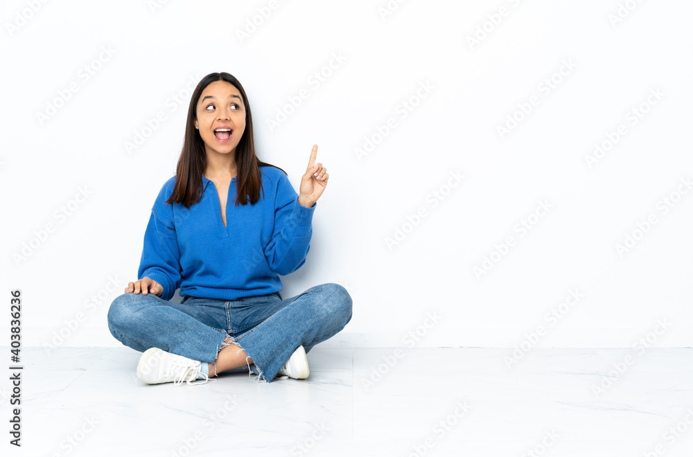 Young mixed race woman sitting on the floor isolated on white background intending to realizes the solution while lifting a finger up Young mixed race woman sitting on the floor isolated on white background intending to realizes the solution while lifting a finger up