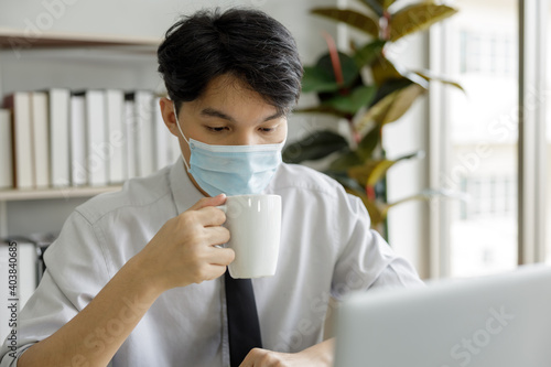 businessman with face mask holding coffee cup in office Thailand