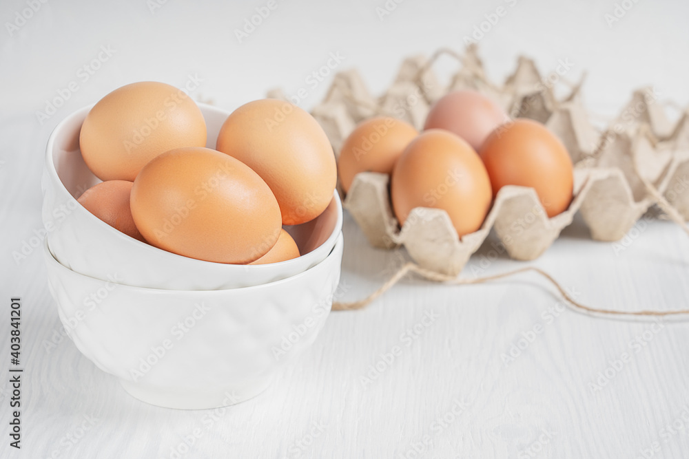 Raw brown fresh chicken eggs in china saucers and container made of recycled paper on white wooden background prepared for easter. Healthy eating and sustainable consumption concept. Horizontal image Raw brown fresh chicken eggs in china saucers and container made of recycled paper on white wooden background prepared for easter. Healthy eating and sustainable consumption concept. Horizontal image