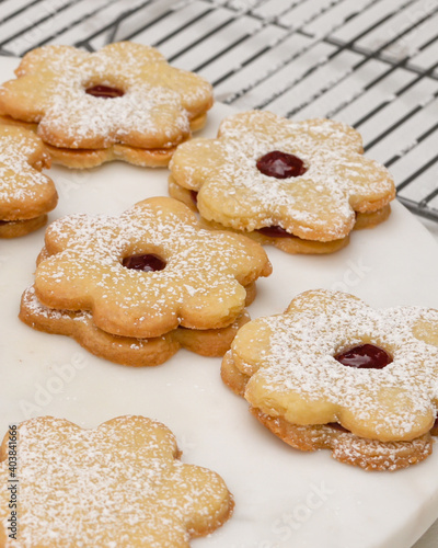 Flower shaped shortbread cookies filled with raspberry jam close up on cooling rack, vertical banner
