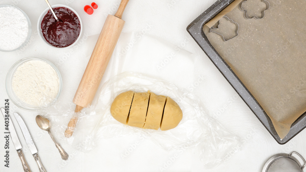 Baking process, food background, flat lay. Shortbread cookie dough, baking pan lined with parchment paper, roller, cookie cutters close up Baking process, food background, flat lay. Shortbread cookie dough, baking pan lined with parchment paper, roller, cookie cutters close up