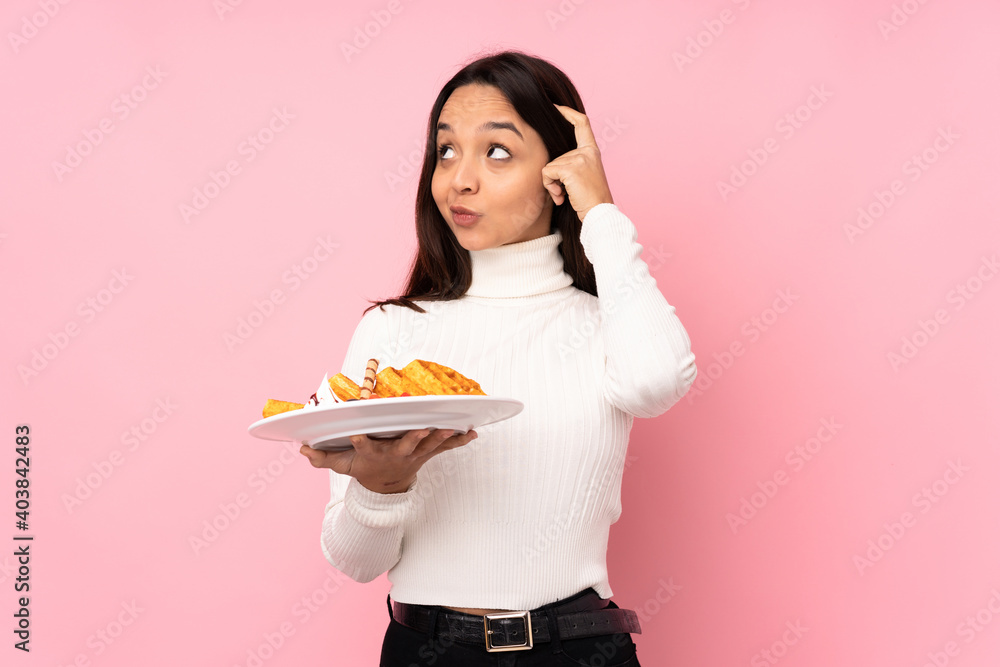 Young brunette woman holding waffles over isolated pink background having doubts and thinking Young brunette woman holding waffles over isolated pink background having doubts and thinking