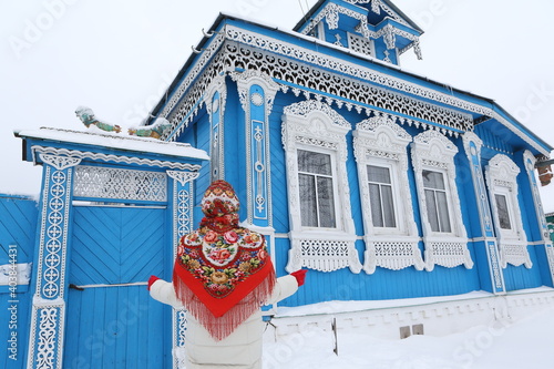 Russian woman in traditional national Pavlovo Posad scarf, shawl. Folk style in architectural fashion, architecture. Vintage wooden rural house, ornamental windows in village in Ivanovo region, Russia photo