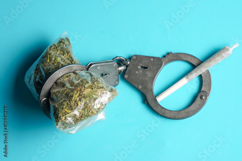 a joint of marijuana and handcuffs on a blue background. Space for copying, space for text.the concept of drug control