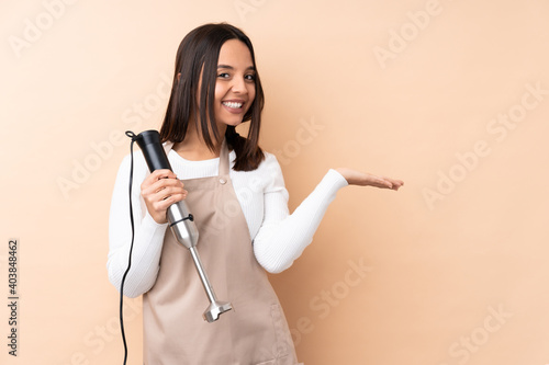 Young brunette girl using hand blender over isolated background presenting an idea while looking smiling towards