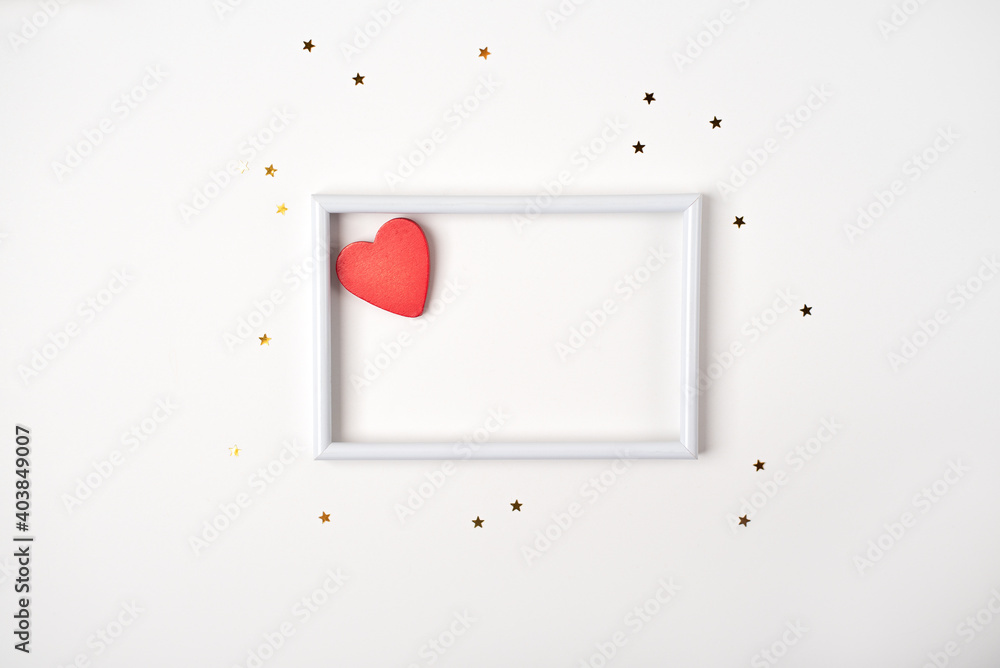 Red wooden heart in the white frame and little golden stars on the light (white) background. Valentine's Day concept. Flat lay, top view. Red wooden heart in the white frame and little golden stars on the light (white) background. Valentine's Day concept. Flat lay, top view.