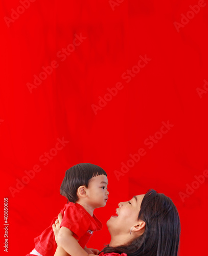 An Asian mother and toddler son (1-year-old) are playing and relax together in red clothing and background for Valentine's theme.