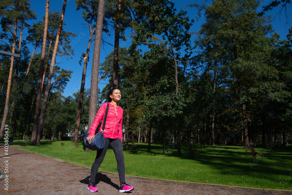 A young woman with a sports bag on her shoulder walks past us in the park. A young woman with a sports bag on her shoulder walks past us in the park.