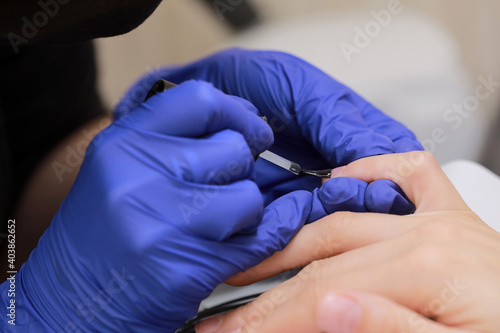 Closeup shot of manicure in a beauty salon. Master during a manicure. Master manicurist varnishes the gel on the nails of a female client. The concept of beauty and health.