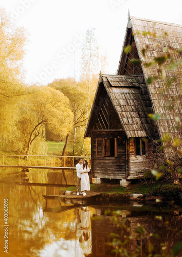 Wooden whimsical cozy house in the autumn park near the lake and a couple in love © Yuliia
