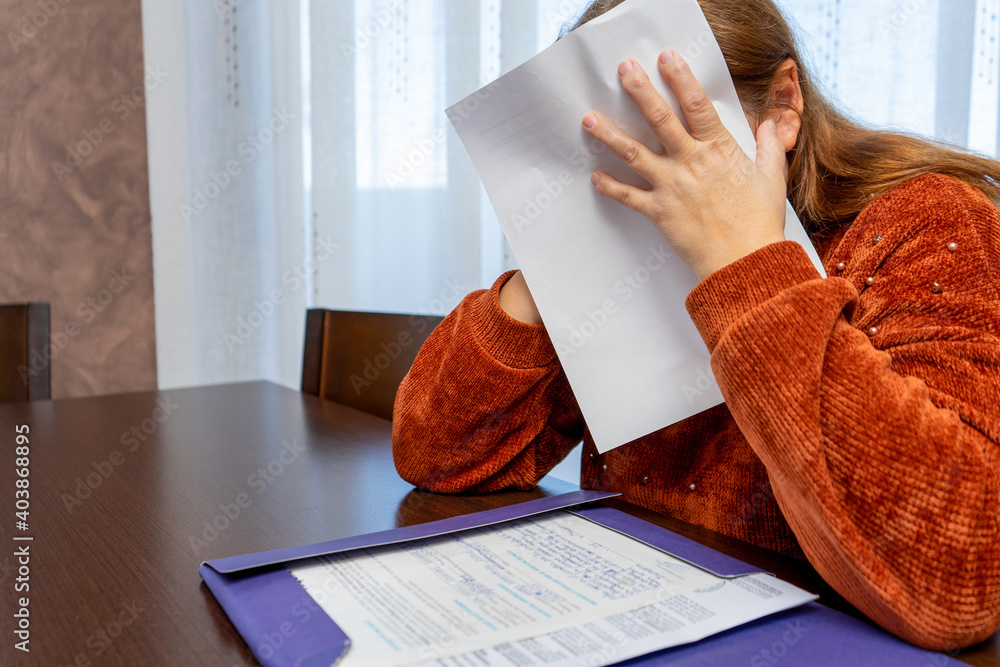 Obraz premium Pretty desperate adult businesswoman reviewing bills at the table in her living room. Selective focus