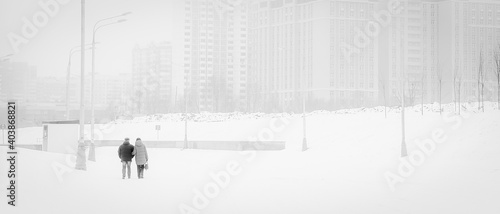 An adult couple walks through a snowy city. horizontal, monochrome Loneliness in a big city.