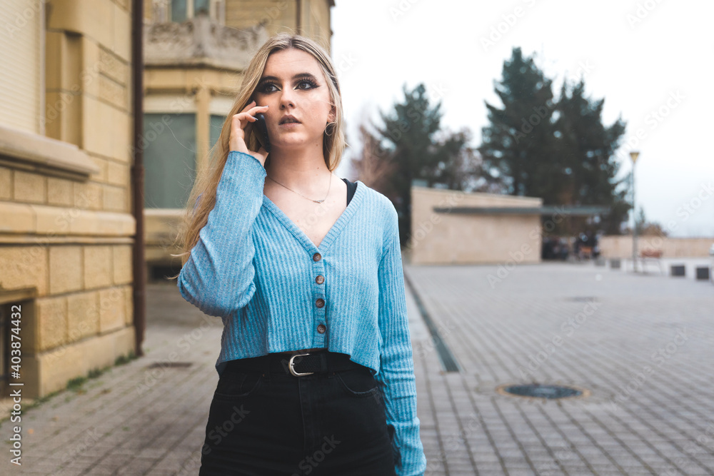 Fototapeta premium Young blonde woman taking by mobile phone on the street