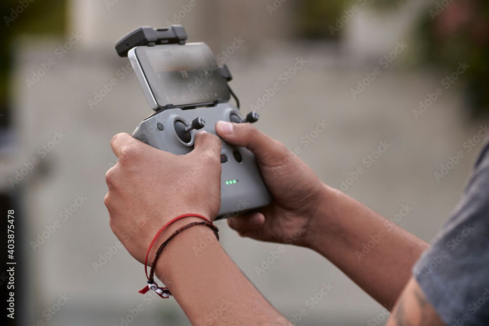 Hands of young man with tattoos controlling a drone watching on his phone