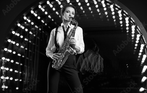 Gorgeous brunette model woman in fashionable formal suit with saxophone