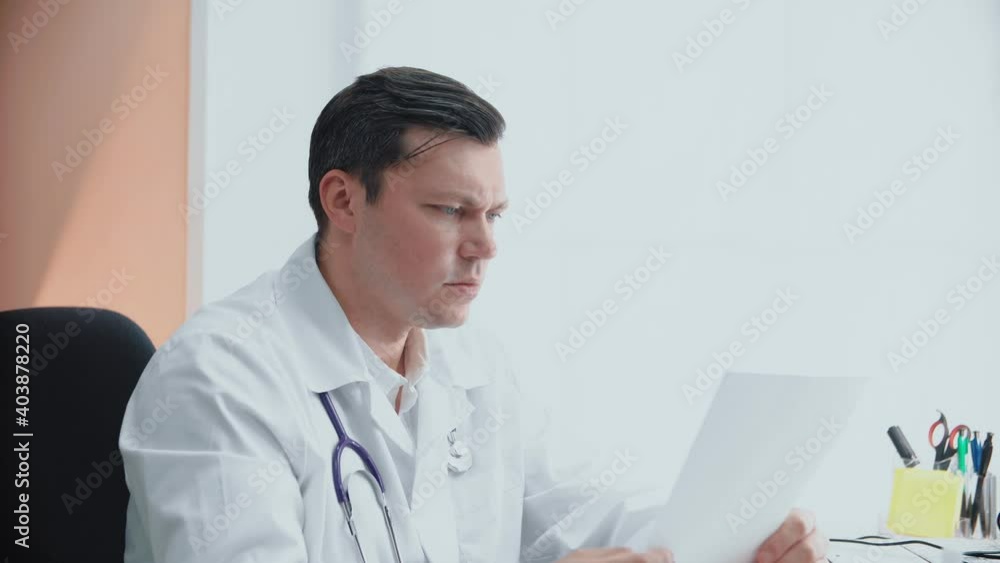 Caucasian doctor sits at a table and examines patient reports in a modern hospital office space. Caucasian doctor sits at a table and examines patient reports in a modern hospital office space.
