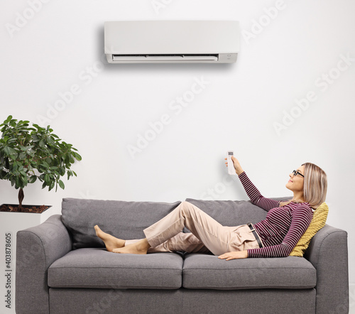 Obraz na płótnie Young woman resting on a gray sofa and holding a remote control from an ac unit