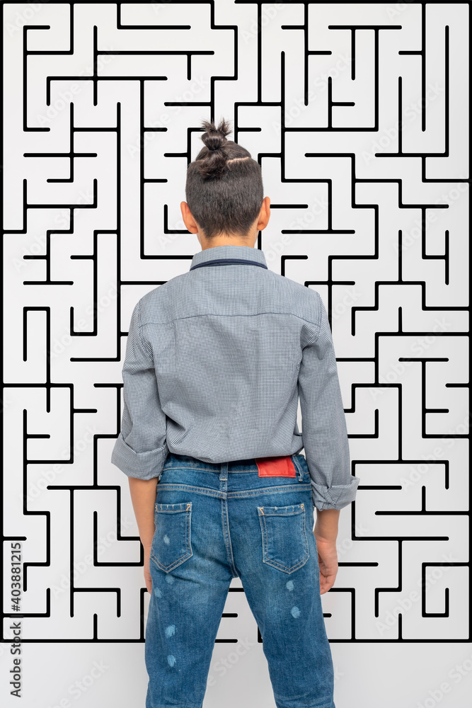 A young boy looks at the maze depicted on the wall and makes a choice or makes a decision. Education concept, growing up A young boy looks at the maze depicted on the wall and makes a choice or makes a decision. Education concept, growing up
