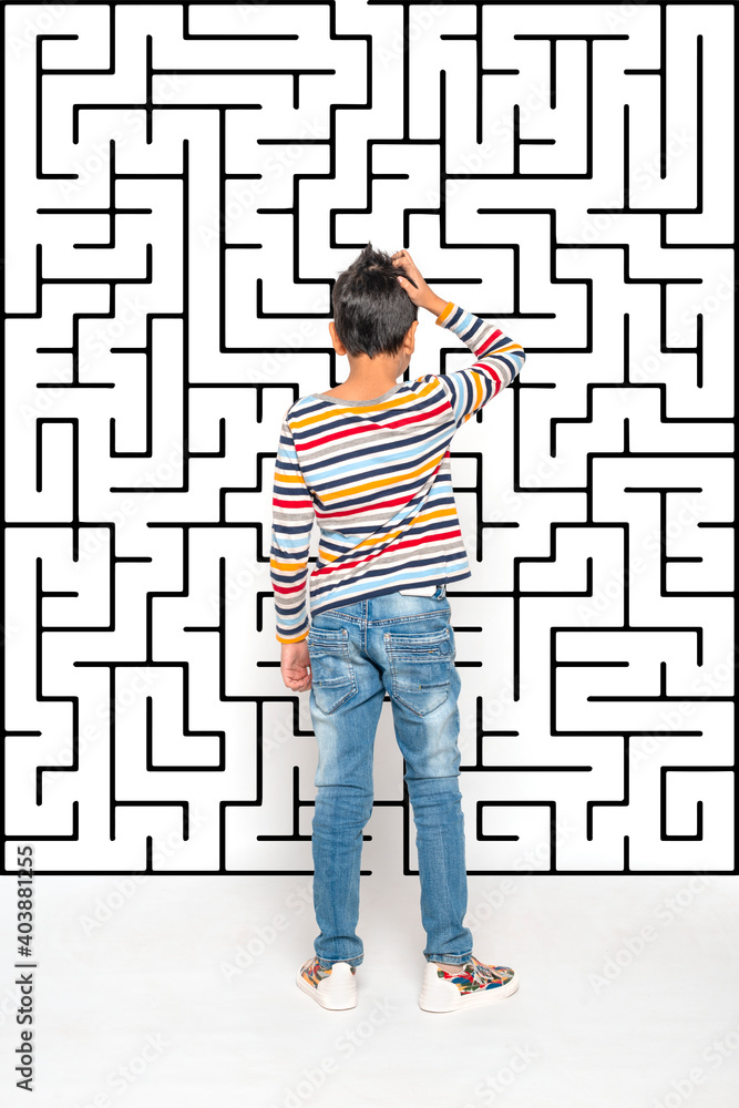 A boy looks at the maze depicted on the wall and makes a choice or makes a decision. Education concept, growing up A boy looks at the maze depicted on the wall and makes a choice or makes a decision. Education concept, growing up
