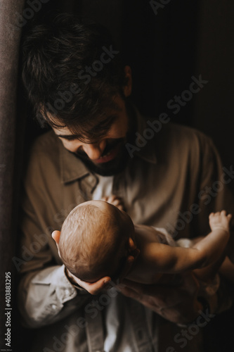 Stylish Caucasian bearded father carrying newborn baby on shoulder. Male man parent holding child daughter son in arms. Authentic lifestyle documentary moment. Single dad family life concept