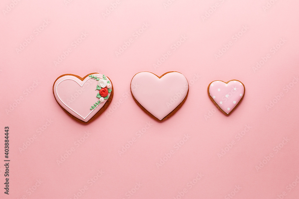 Three heart shaped gingerbread cookies in a row on pink background. Overhead view, copy space. Valentine's Day concept