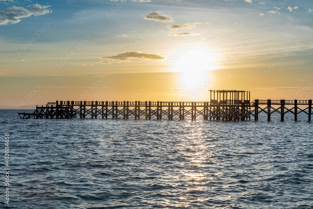 silhouette of a wooden jetty at sunset with blue soft waves in the fore ground