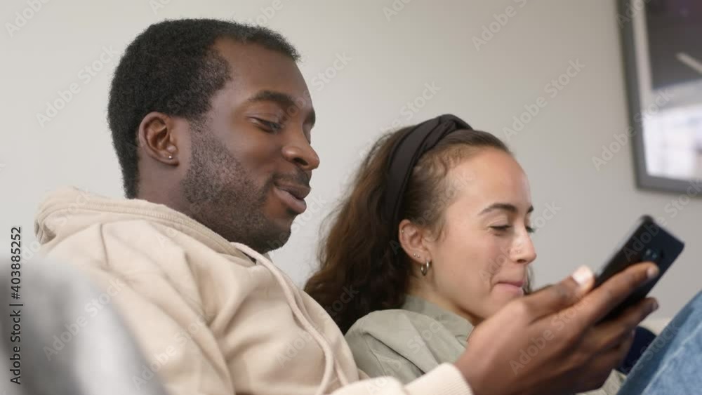 Young Smiling Couple Relaxing At Home Sitting On Sofa Checking Social Media On Mobile Phones Together Young Smiling Couple Relaxing At Home Sitting On Sofa Checking Social Media On Mobile Phones Together