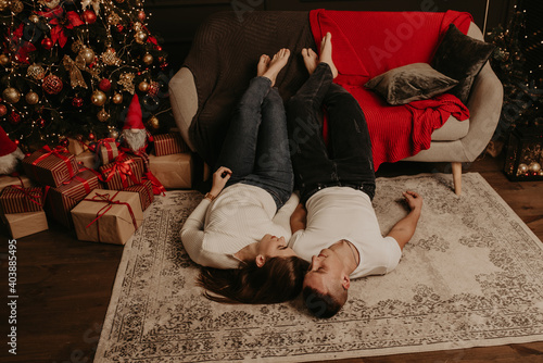 ouple lie on floor near couch with legs up kissing in the bedroom near christmas tree © Andrii
