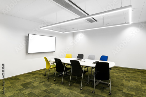 Mała sala konferencyjna w korporacji z monitorem na ścianie, krzesłami, stołem oraz zieloną podłogą