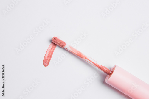 peach lip gloss is smeared on a white background, next to a drop of lip gloss is an applicator