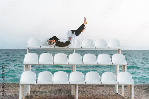 A young woman lies on the podium and the sea and lifted her legs up, leaning against an invisible wall