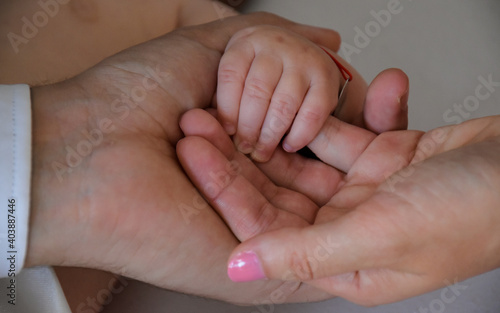 Close-up of dad and mom holding the little hand of their newborn. The photo symbolizes the unity, love and affection the parents have for their new baby.