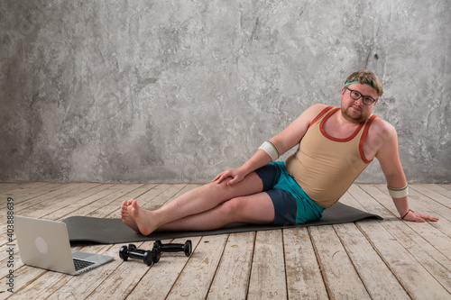  overweight man exercising, doing stretching exercises on yoga mat, watching fitness videos online on laptop at home. yoga exercises online with laptop