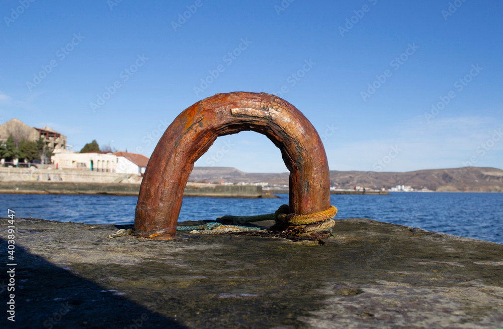 An old rusty metal device for mooring a boat on a sea pier. An old rusty metal device for mooring a boat on a sea pier.