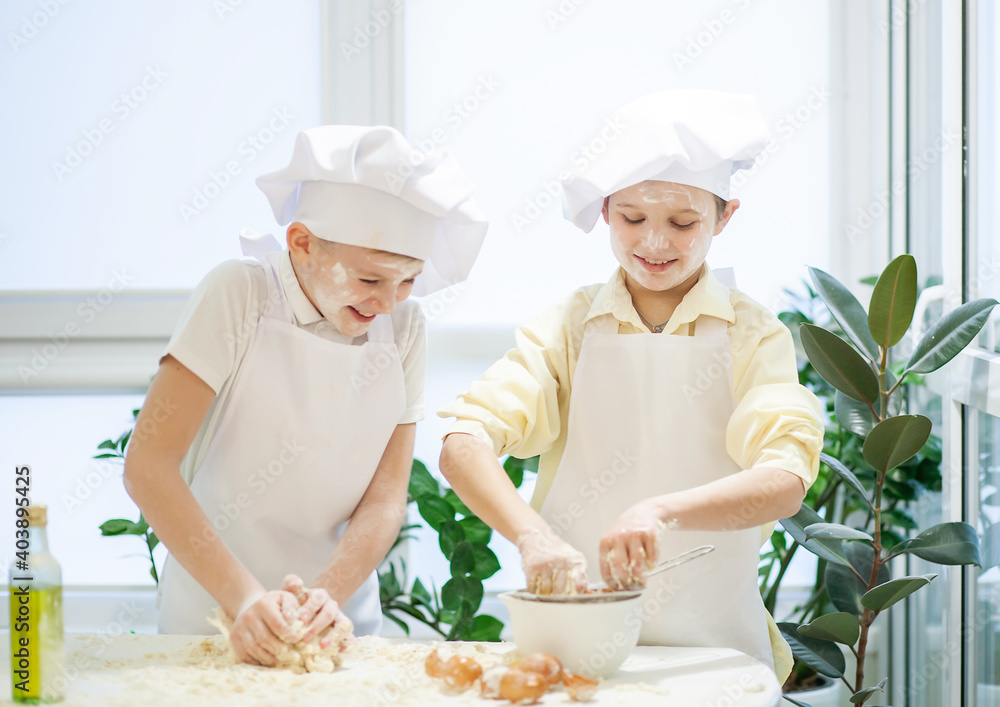 Two cute European boys dressed as a cook are kneading flour, milk and ...